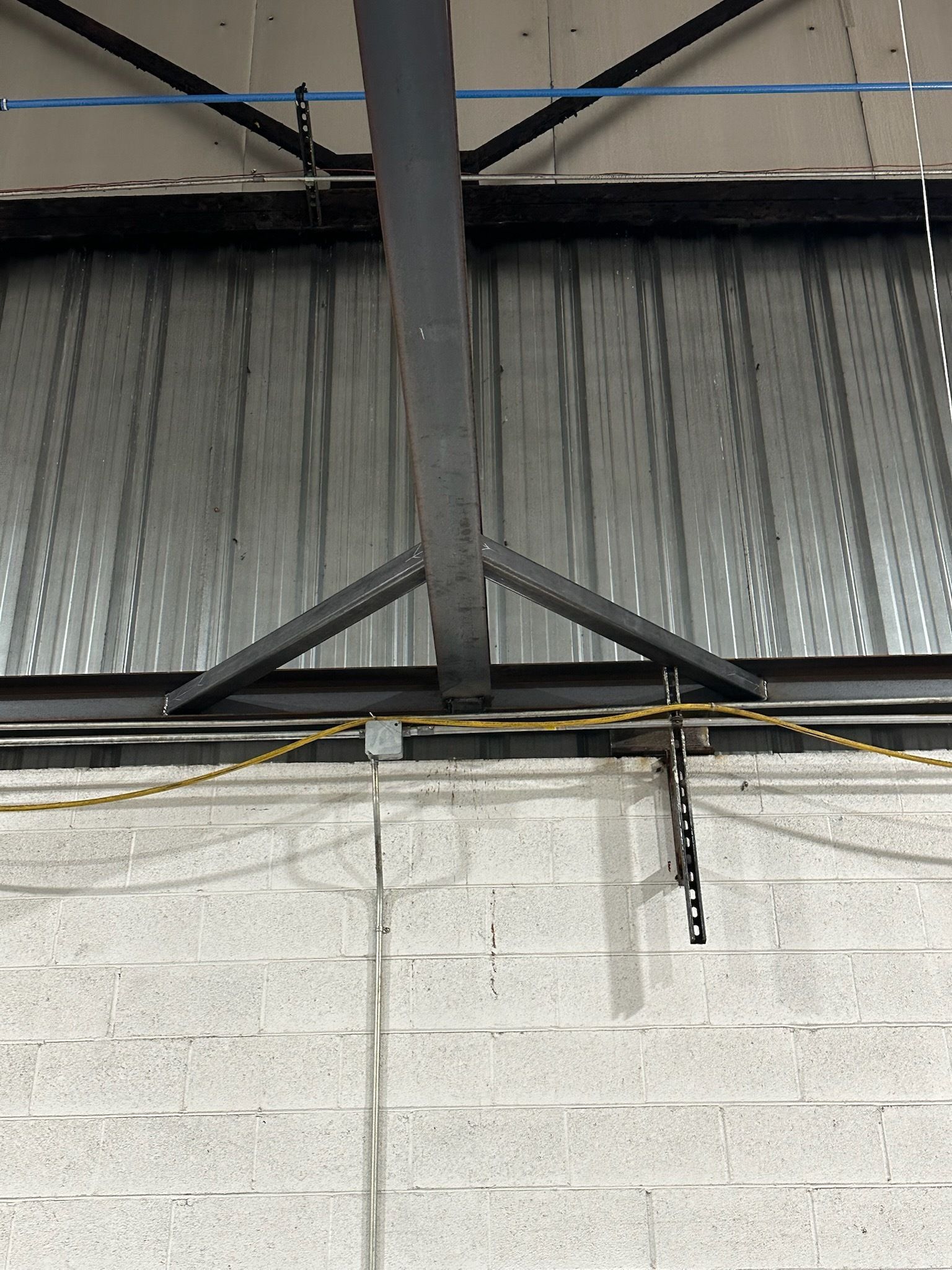 Gray metal beam and support over a brick wall, with corrugated metal above.