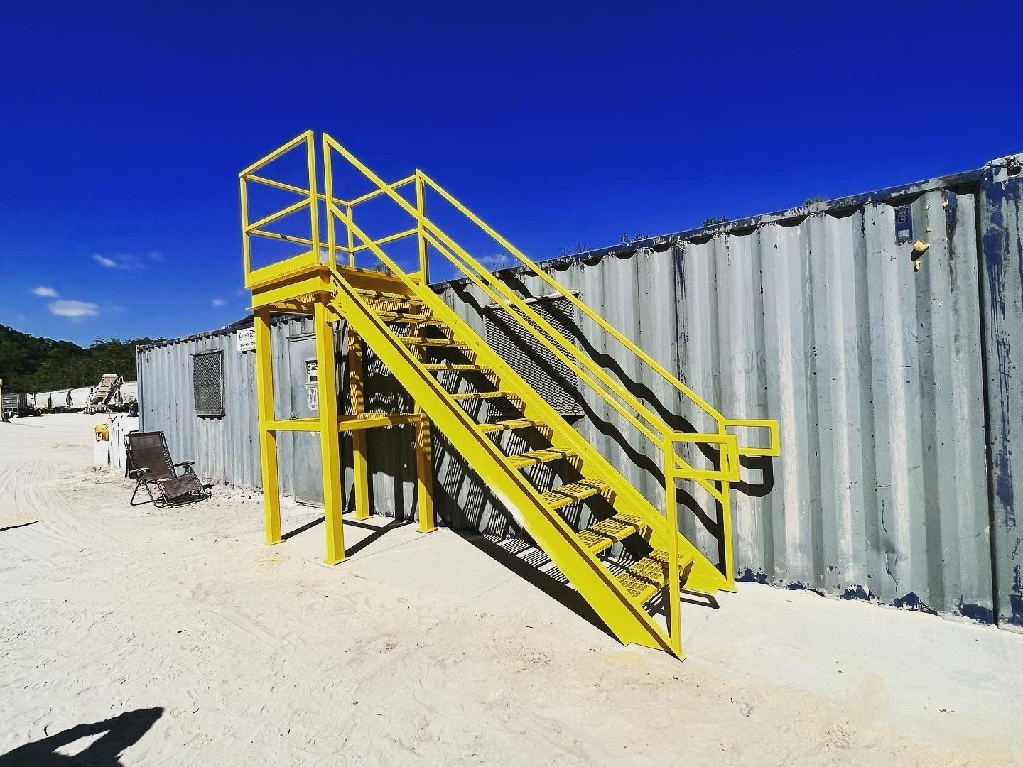 Yellow metal staircase leading up to a container building against a bright blue sky.