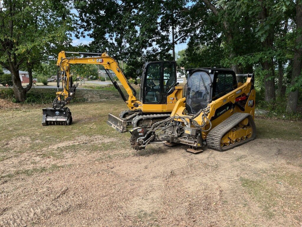 Two yellow construction vehicles on woodchips; excavator and skid steer with attachments.