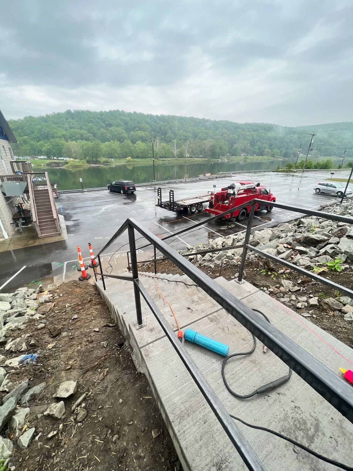 Concrete stairs with railing lead down to a parking lot next to a river; a red fire truck is parked.
