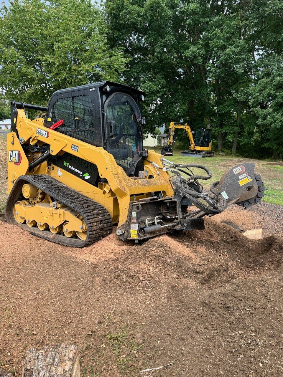 Yellow CAT skid steer with a stump grinder attachment, grinding a tree stump.