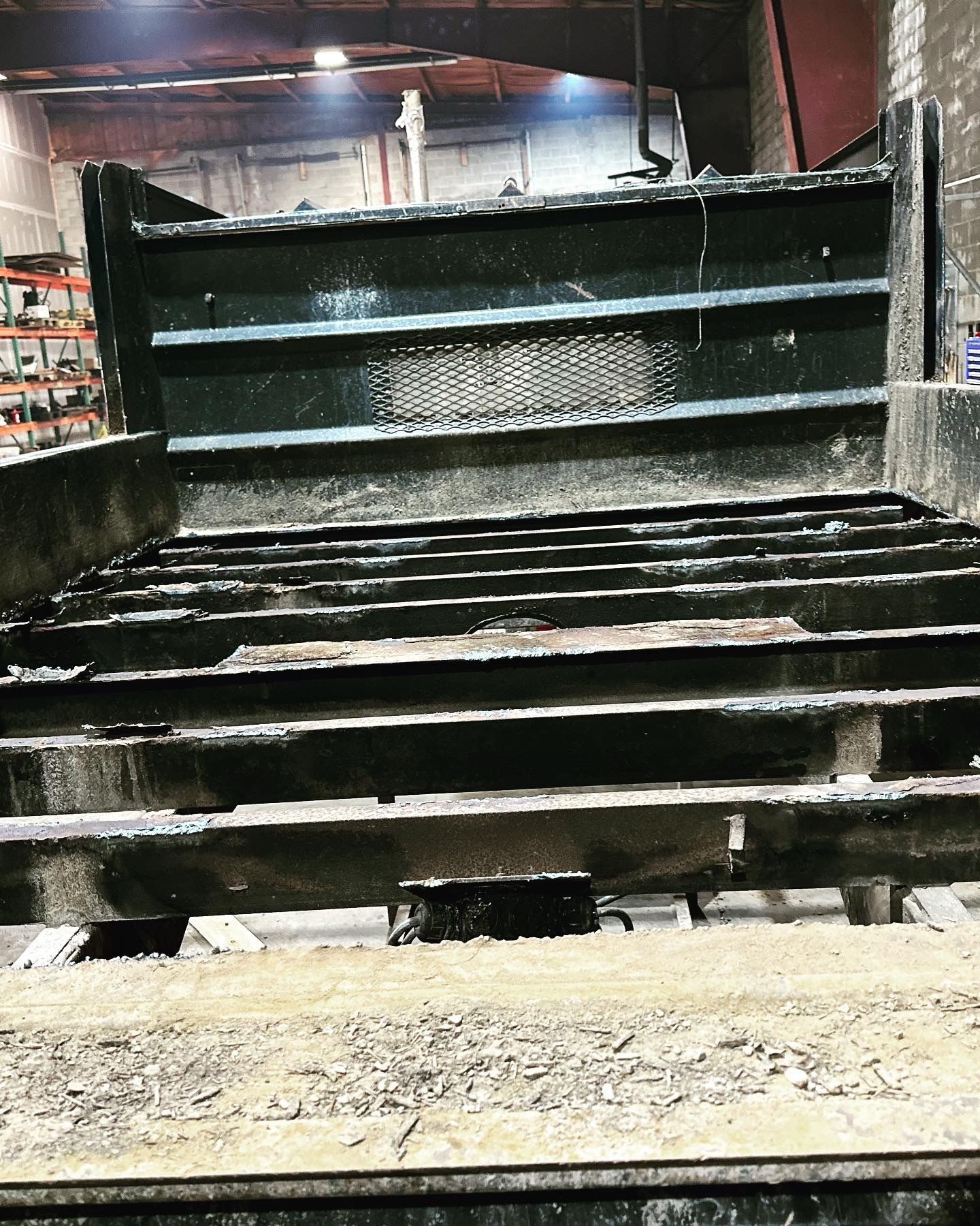 A dump truck bed, empty, viewed from the back. Black metal slats with some debris.