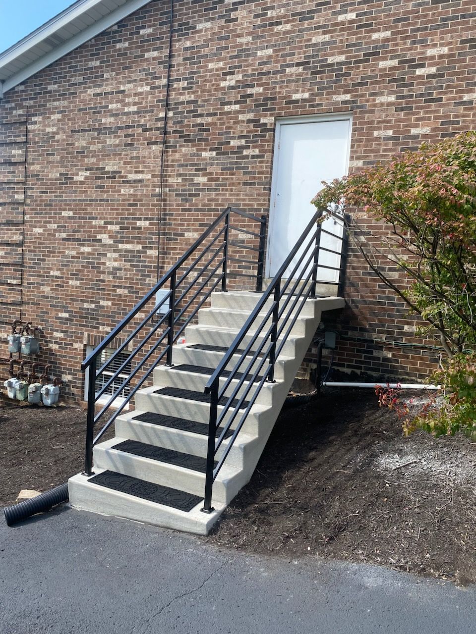 Staircase with black handrails and a white door against a brick building. Ground is covered with mulch.