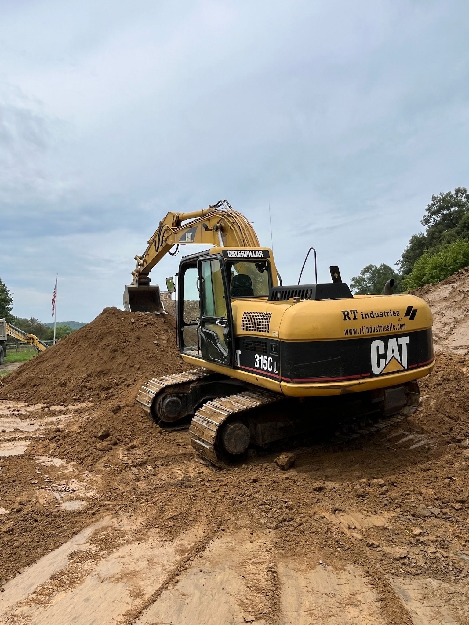 Yellow Caterpillar excavator digging in dirt; cloudy sky.