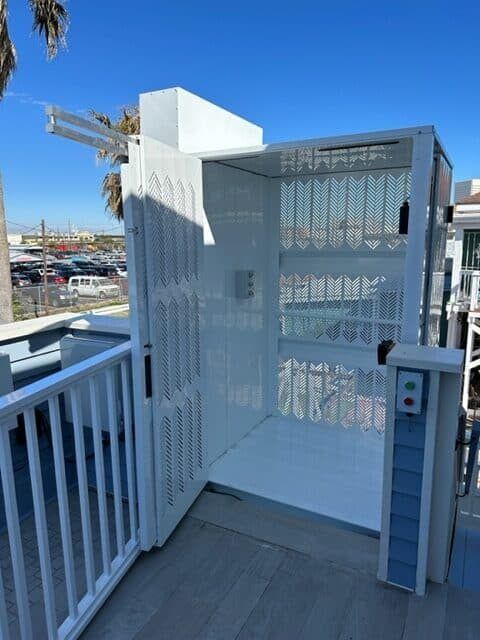 White elevator lift on a balcony with blue accent. Exterior shot on a sunny day.
