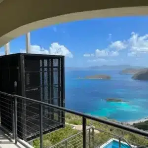 Balcony with an enclosed elevator lift overlooking a tropical ocean view with islands.