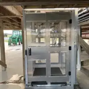 Metal and clear paneled elevator-like structure, under a wooden structure; tractor in the background.