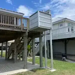 Beach house with an elevator lift for accessibility. Wooden structure, gray lift, grass.