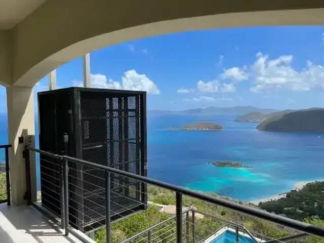 Black elevator lift on a balcony with ocean view. Islands and blue water are in the background.
