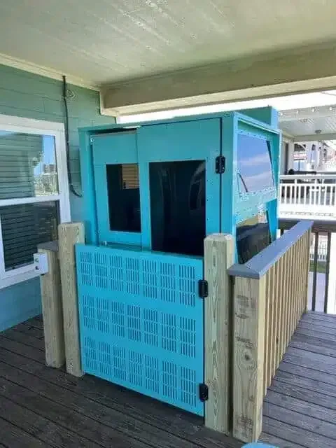 Turquoise elevator lift enclosed in a blue and wood structure on a deck.