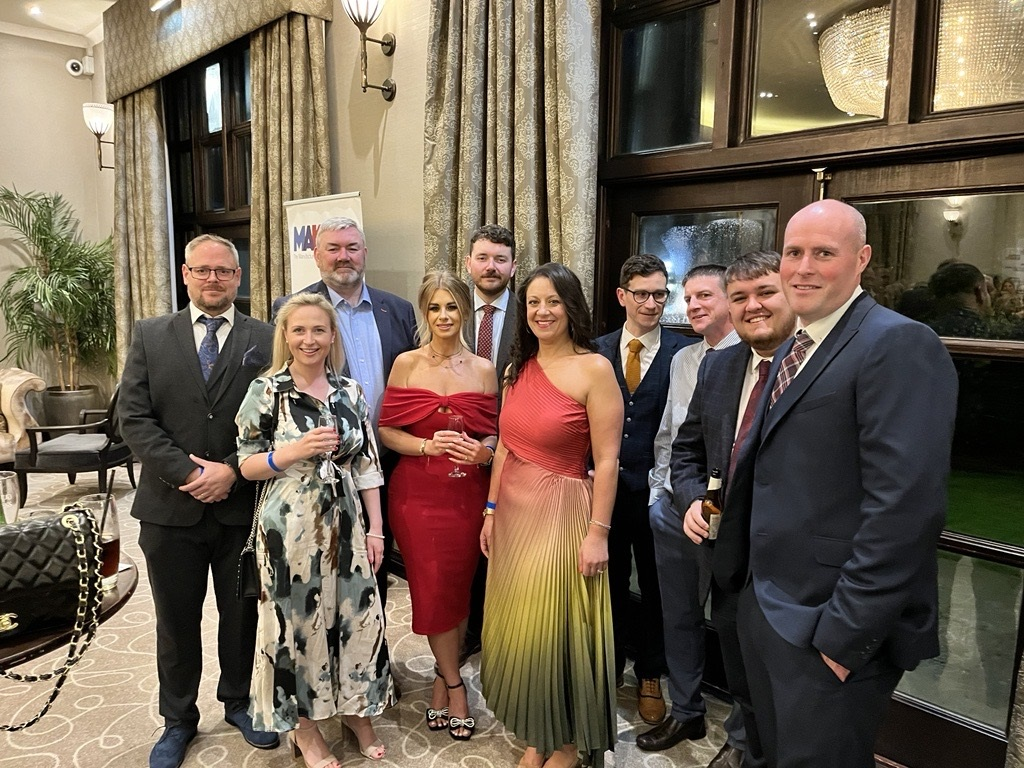 Group of people in formal attire pose for a photo indoors, likely at an event.