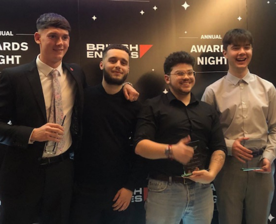 Four men in formal wear at an awards night, smiling and holding trophies.
