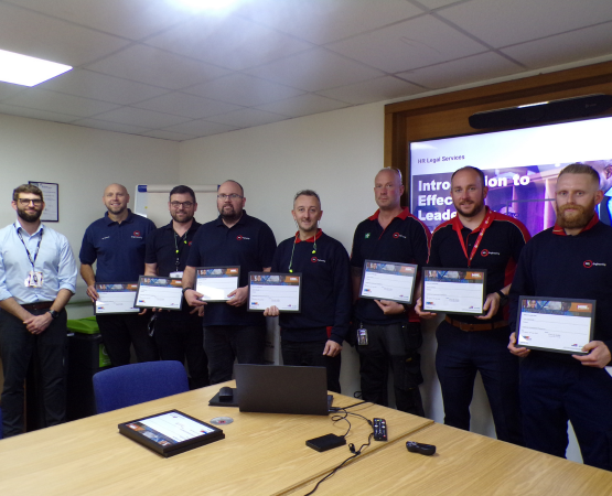 Group of men holding certificates in an office, celebrating leadership training completion.