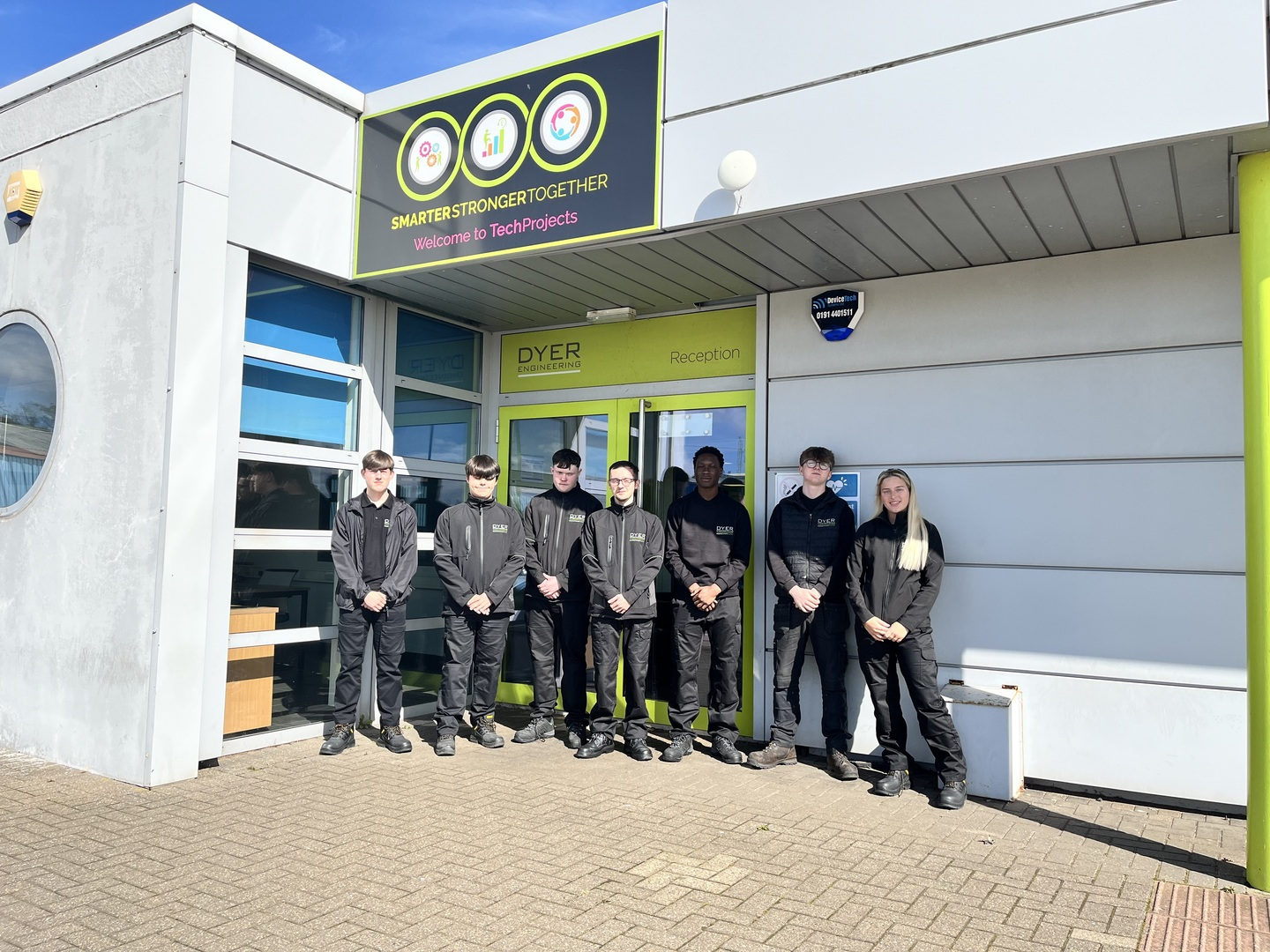 Group of uniformed individuals standing outside a building with a sign.