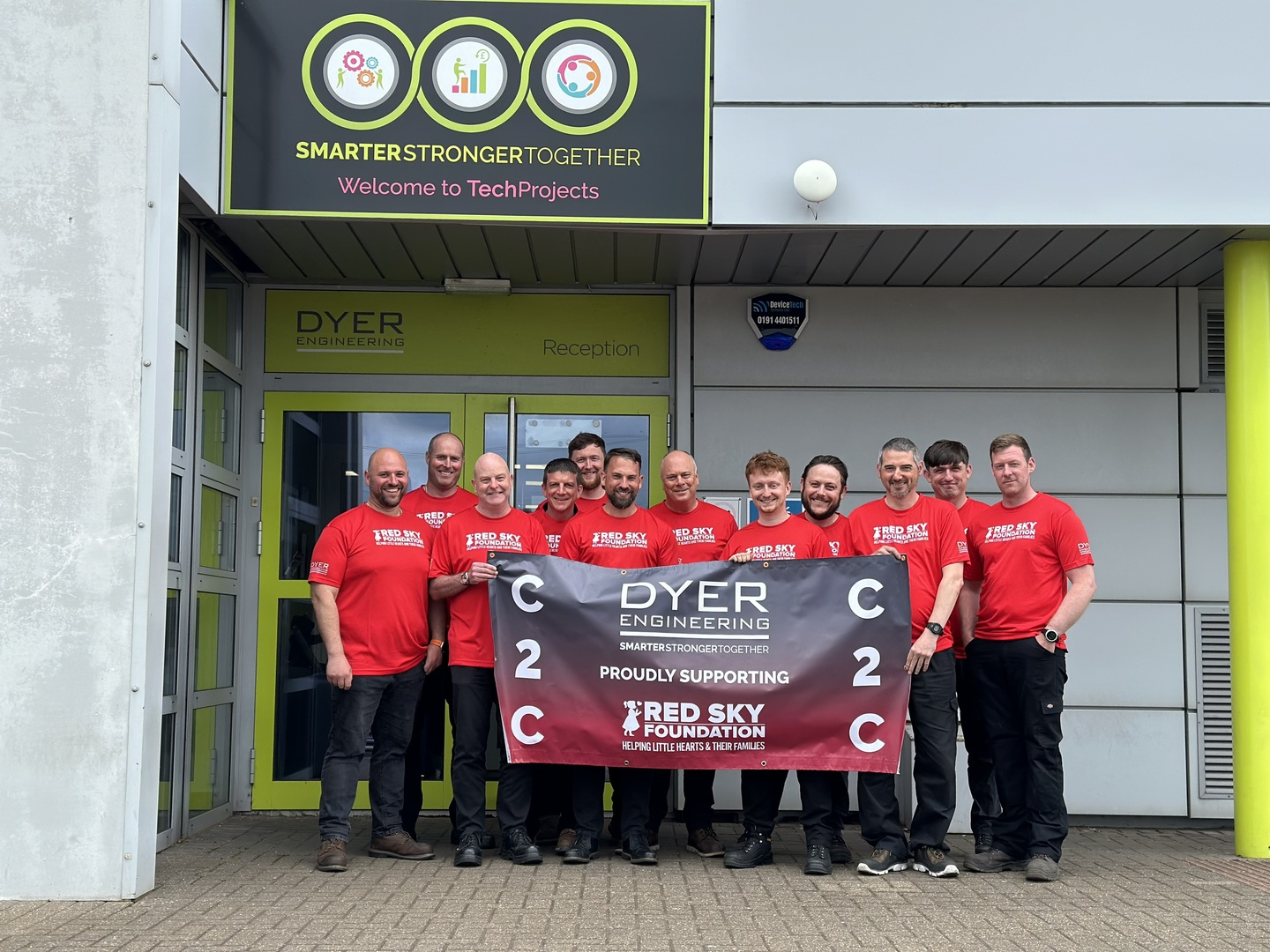 Group of men in red shirts holding a banner outside a building.
