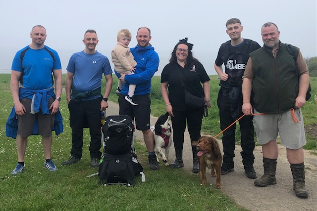 Group of people and dogs on a path in a grassy field on a foggy day.
