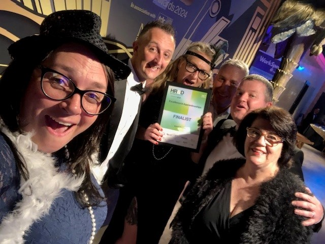 Group of people celebrating and holding an award, dressed up, smiling in a well-lit, party-like setting.