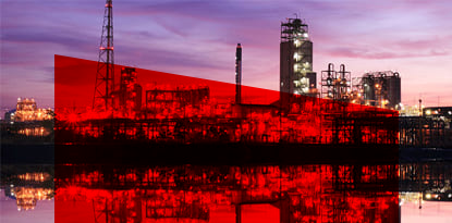 Industrial plant silhouetted against a colorful sunset sky, with reflections in the water.