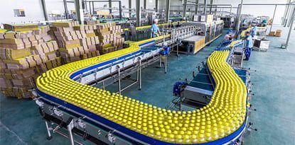 Bottling factory: yellow bottles on a conveyor belt wind through a large industrial space.