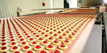Rows of cherry-topped cookies on a conveyor belt in a factory.
