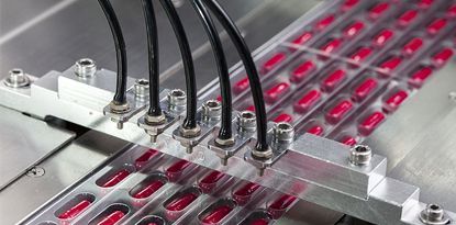 Pharmaceutical manufacturing machine filling blister packs with red capsules.