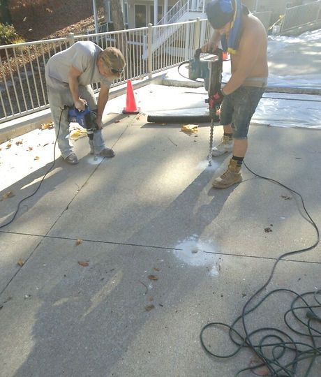 Two men are working on a concrete surface with a drill