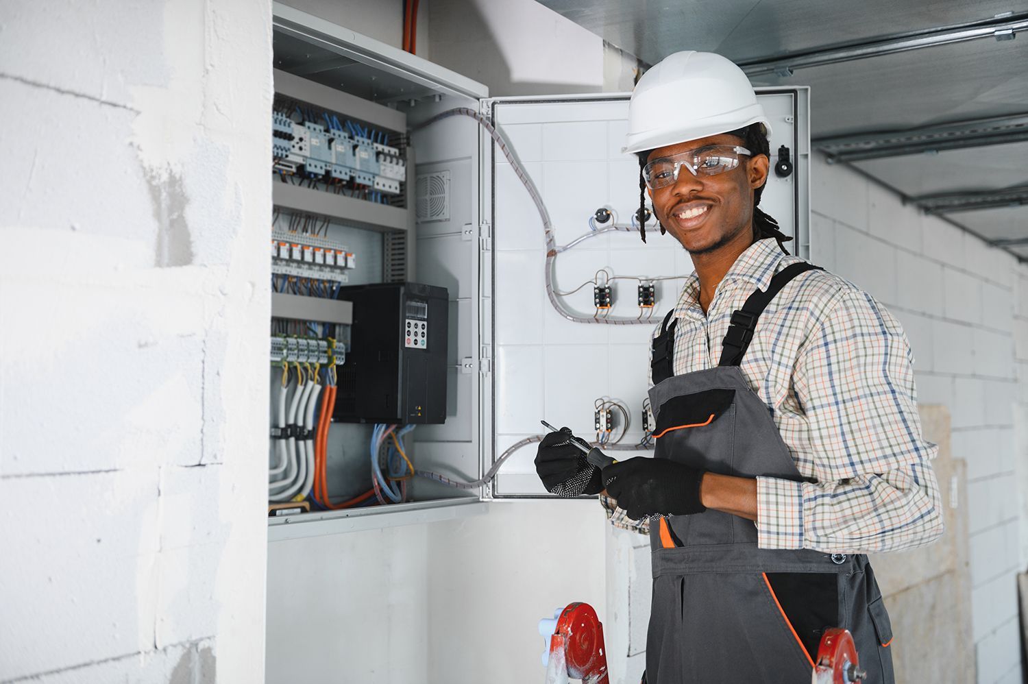 Commercial electrician working on control panel in building under construction.