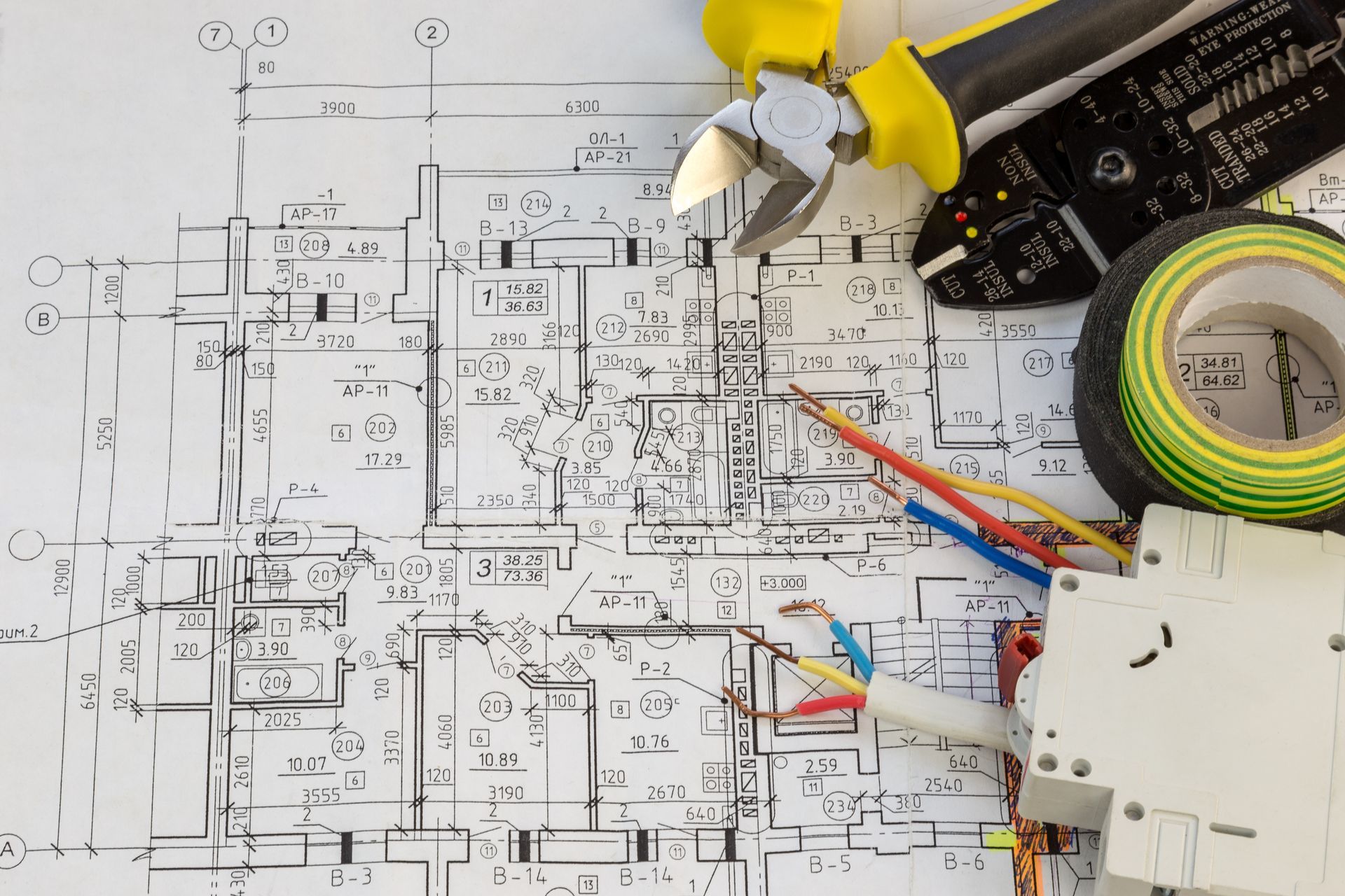 Electrical tools and wires placed on top of a detailed home wiring blueprint.