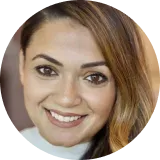 Woman with brown hair smiling, wearing a light-colored top.