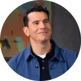 Man in a blue jacket smiles, looking upward. Background includes colorful artwork.