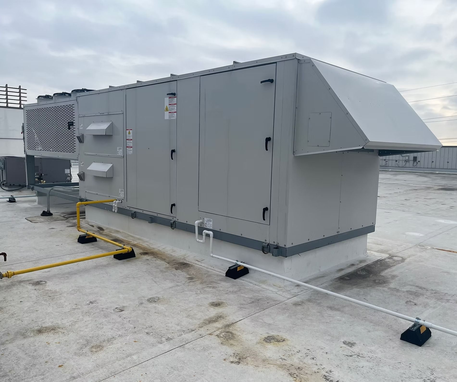Large, gray rooftop HVAC unit on a flat roof with metal ductwork and a yellow gas line.