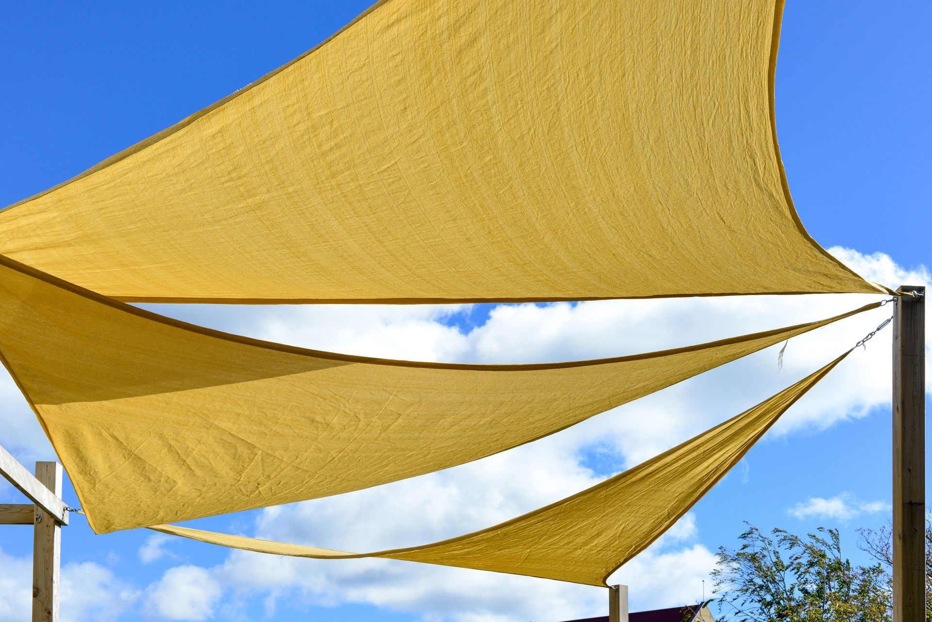View of a yellow shade sail against a blue sky with some clouds.