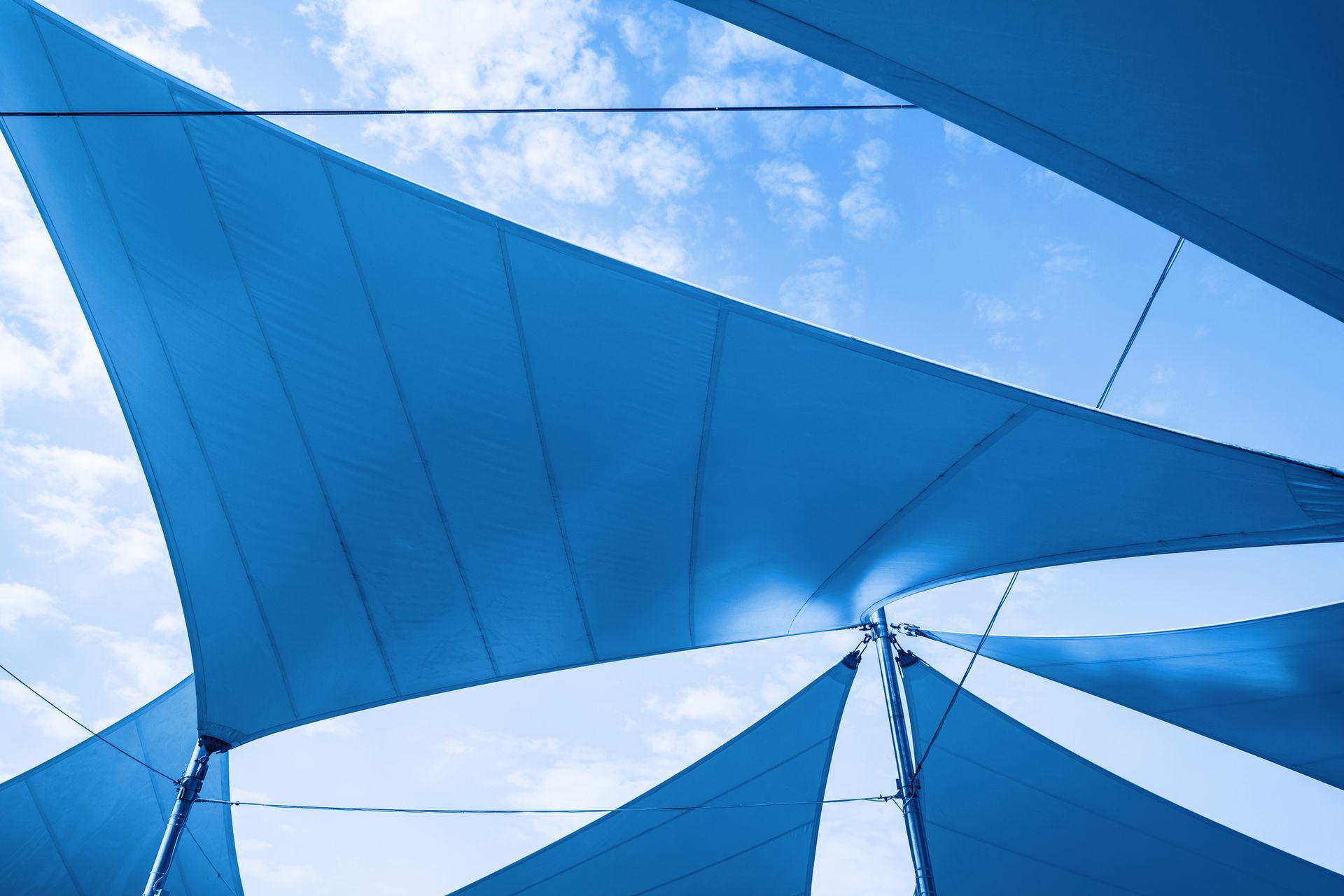 Blue shade sails billowing with blue sky background, representing shade repair services.