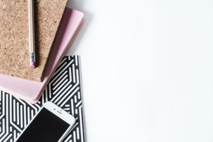 A cell phone , notebooks , and a pencil on a white table.