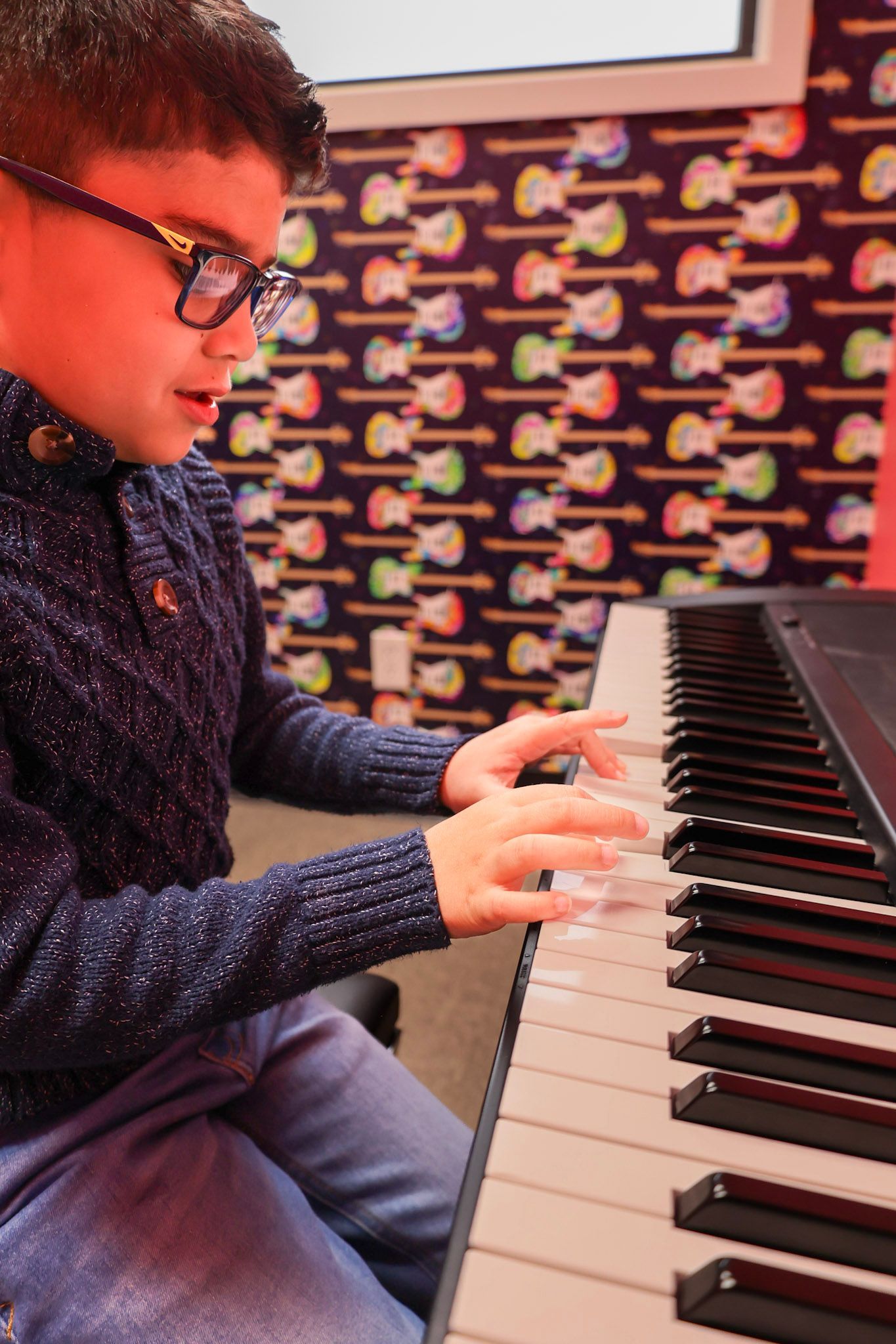 A young boy is sitting at a keyboard and smiling.
