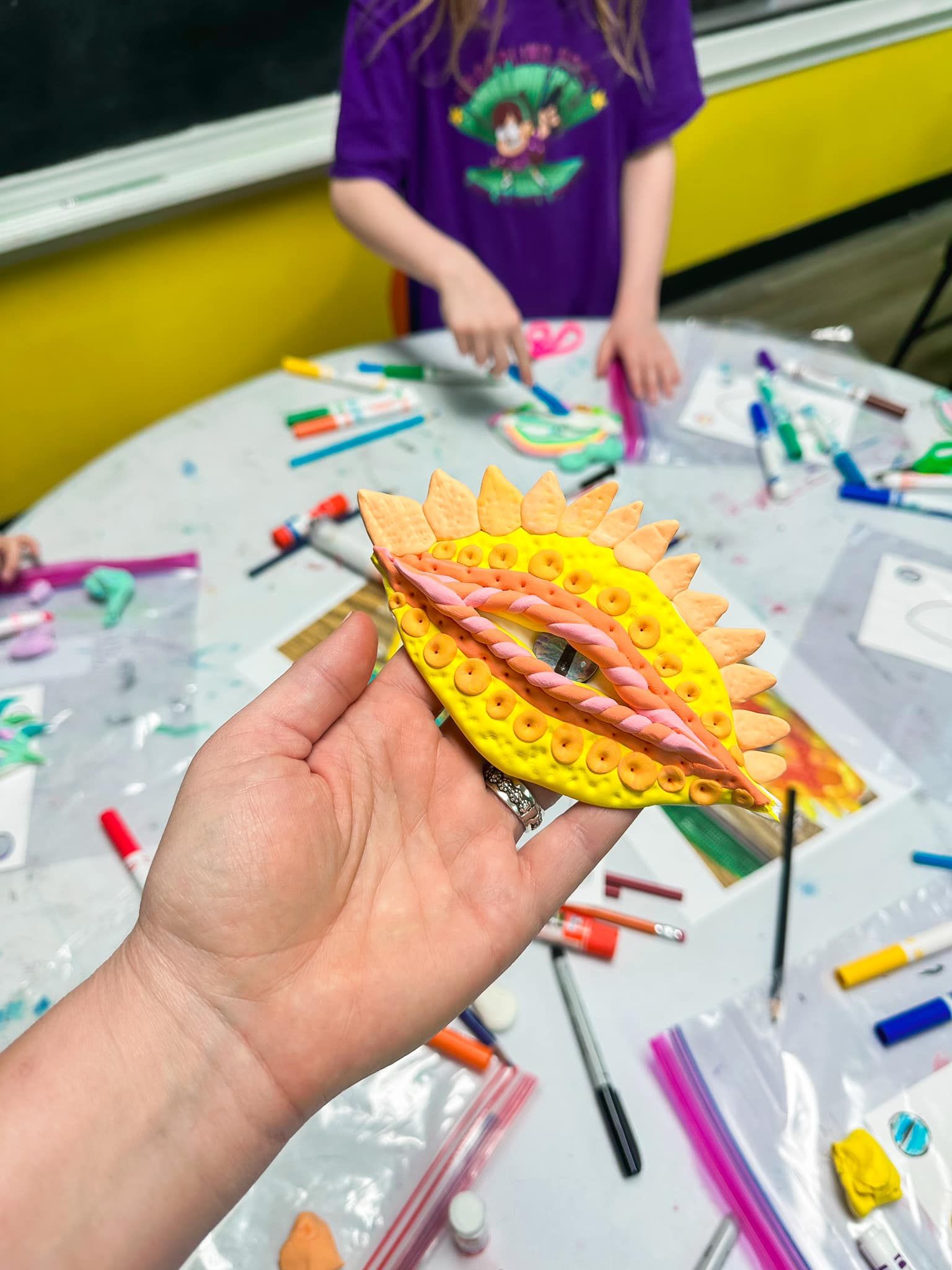 A little girl is holding a package of stickers in front of a shelf.