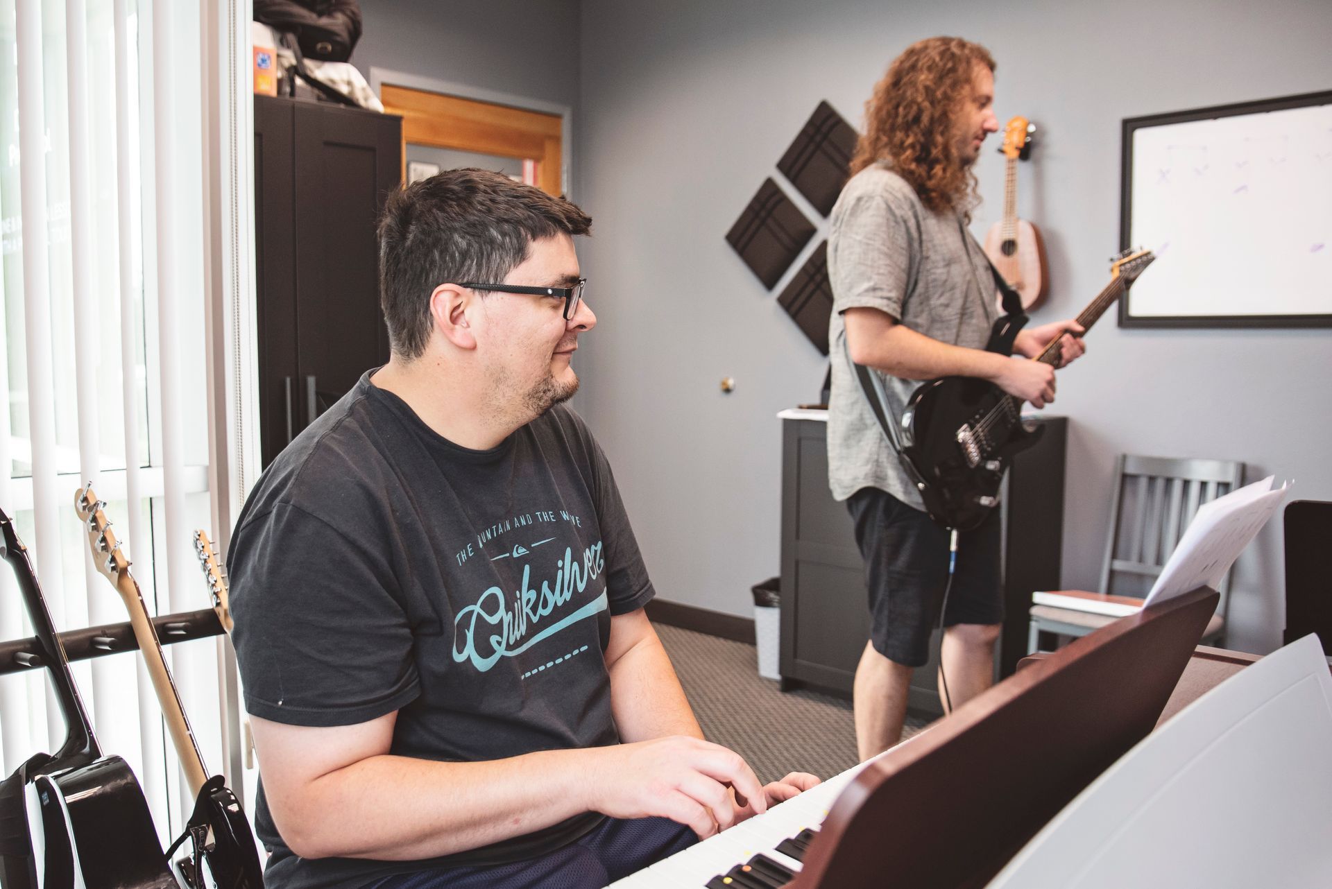 A man is sitting at a piano while another man plays a guitar.