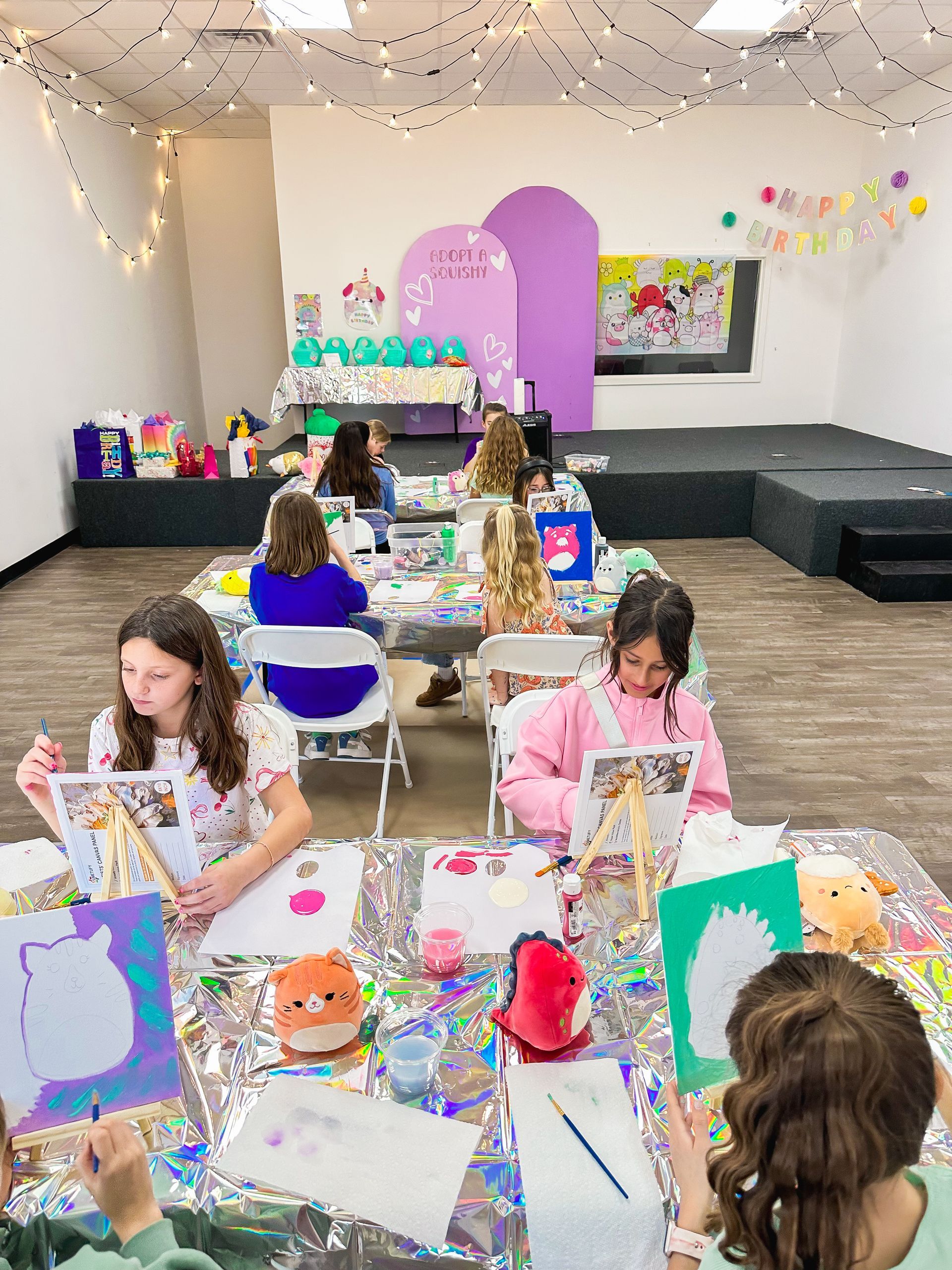 A group of children are sitting at tables in a room painting.