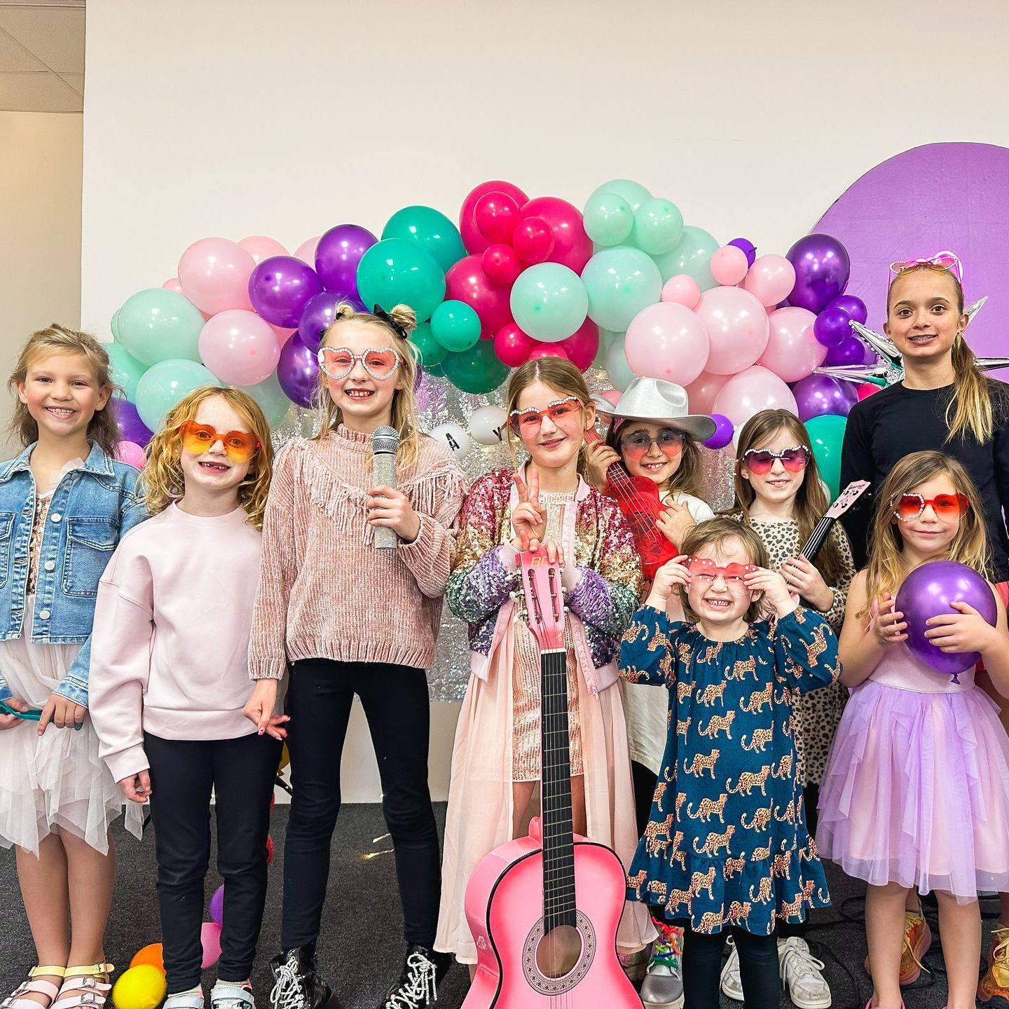 A group of young girls are posing for a picture with balloons and a guitar.