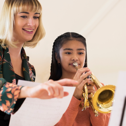 A woman is teaching a young girl how to play a trumpet