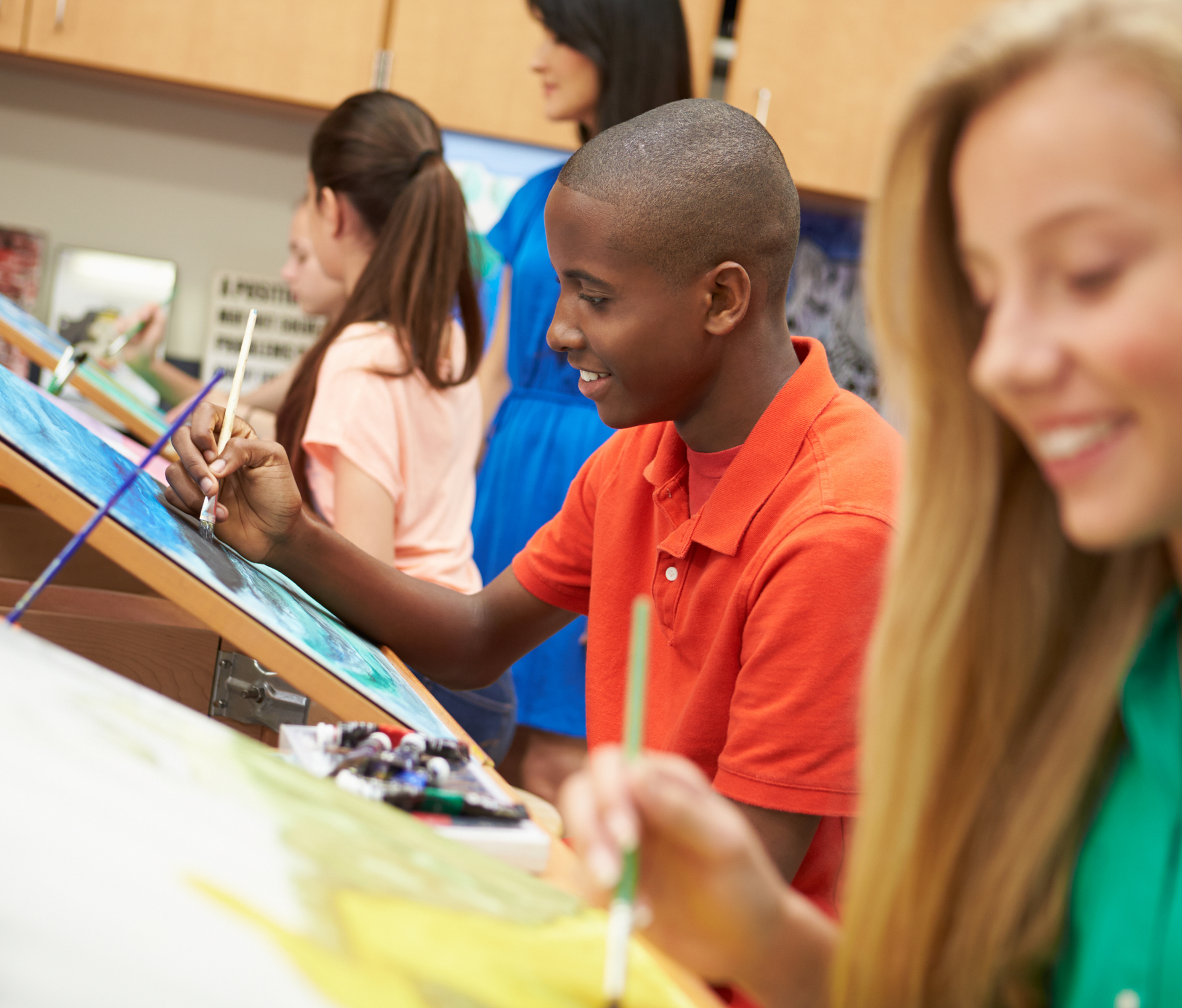 A group of young people are painting on canvases in a classroom