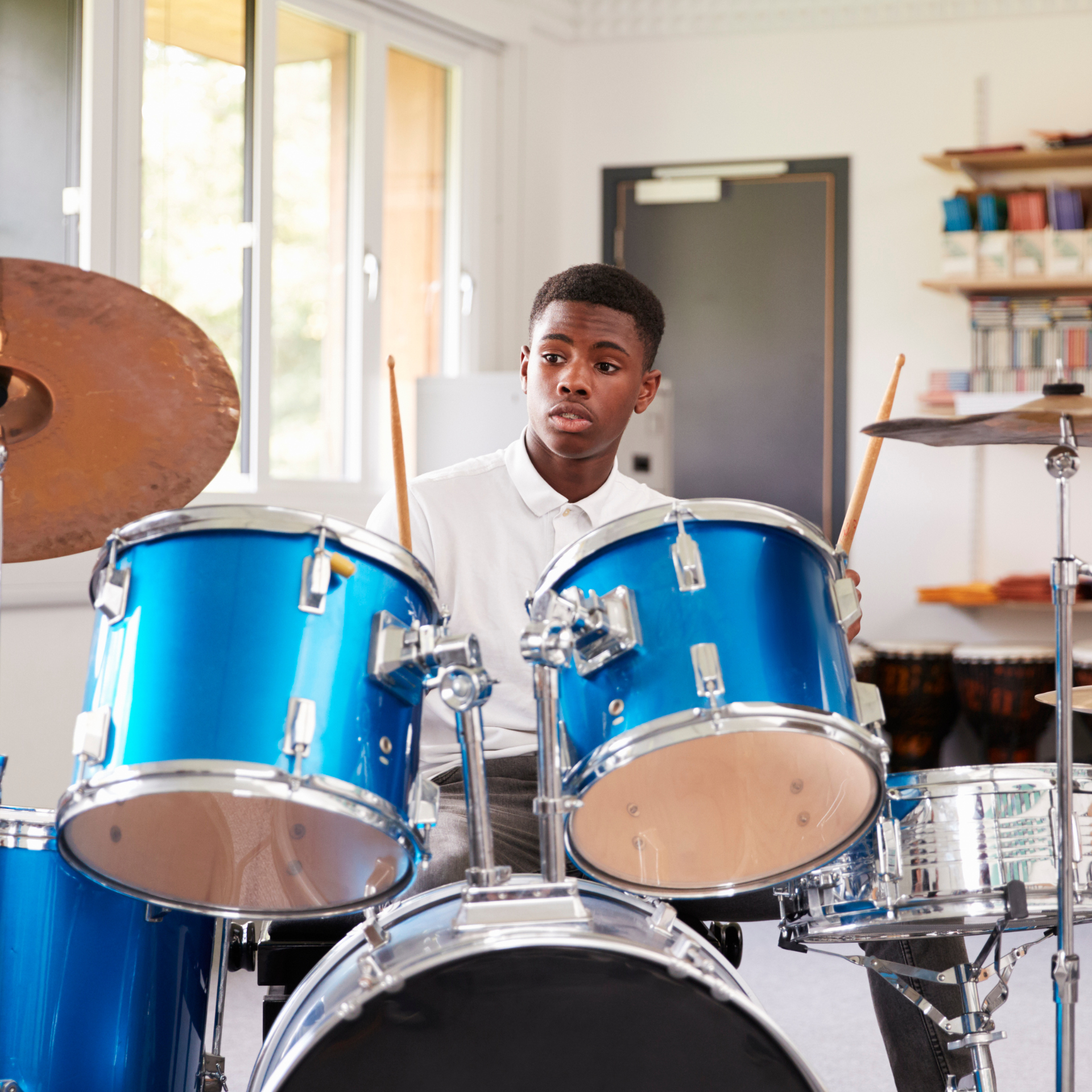 A young man is playing drums in a room.