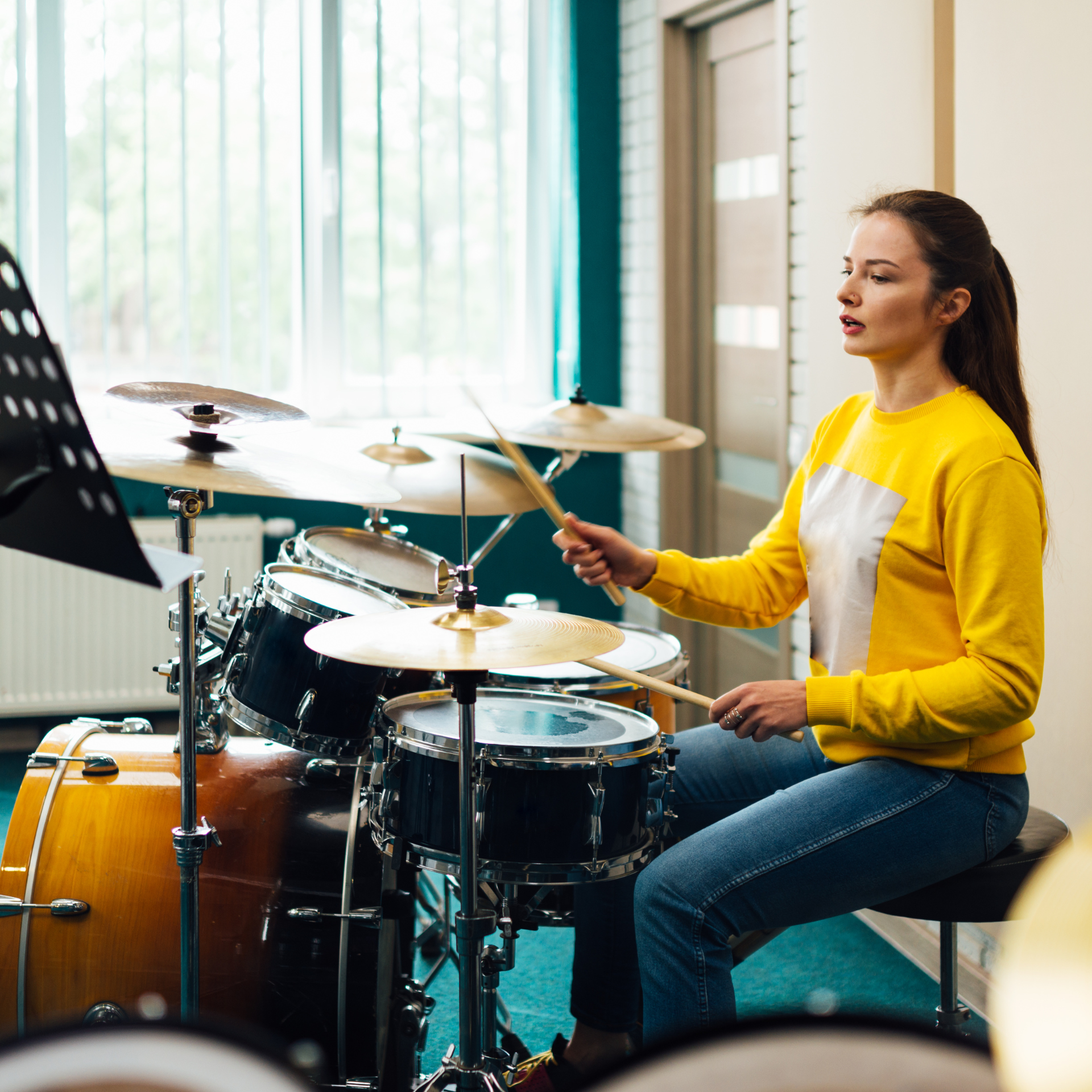 A woman in a yellow shirt is playing drums in a room.