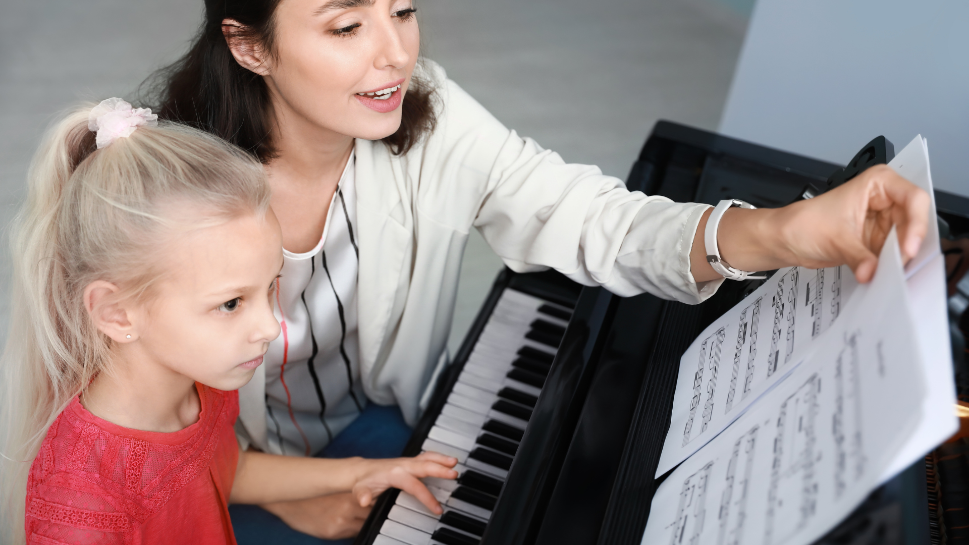 A woman is teaching a little girl how to play the piano.