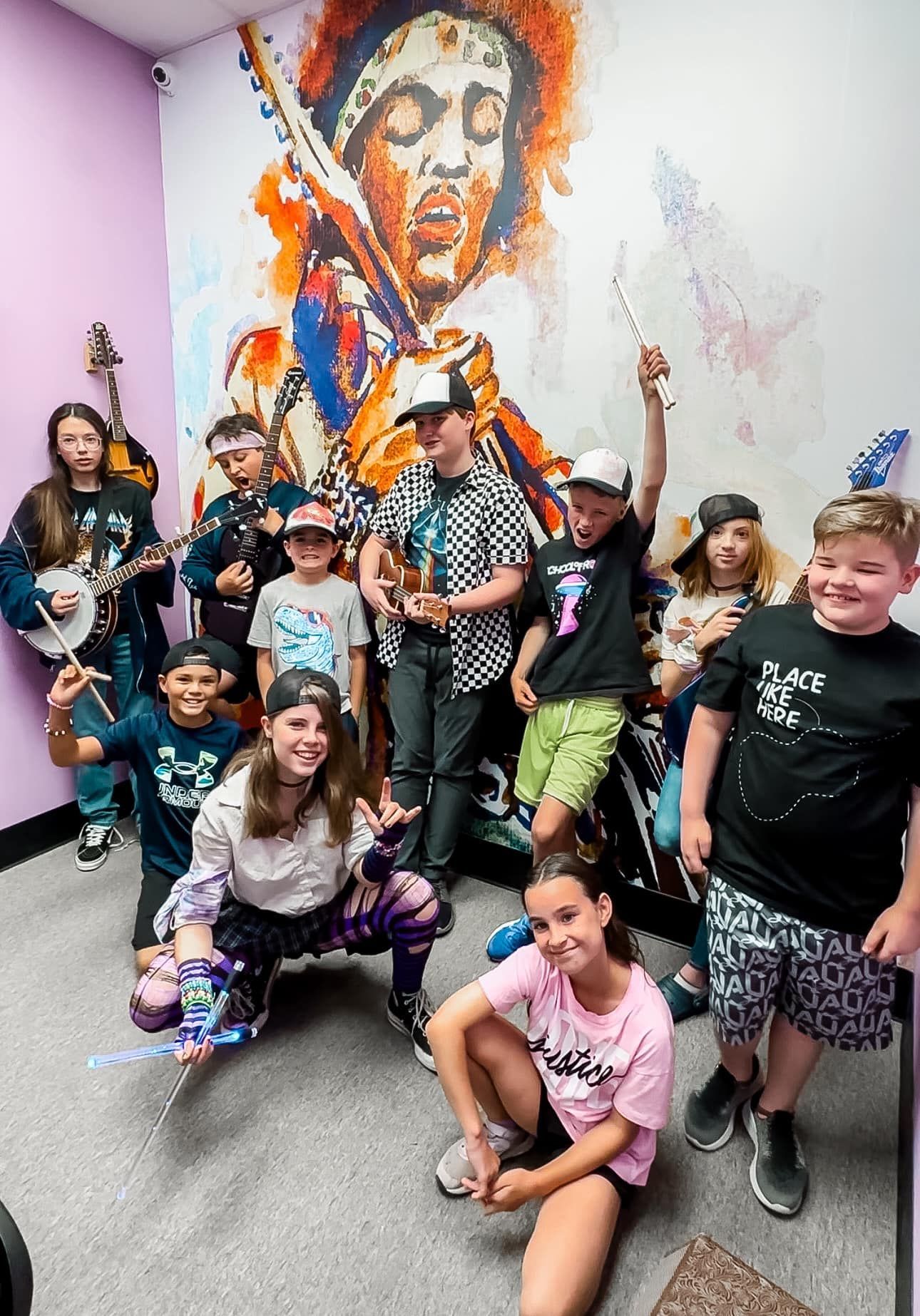 A group of young people are posing for a picture in front of a mural of jimi hendrix.