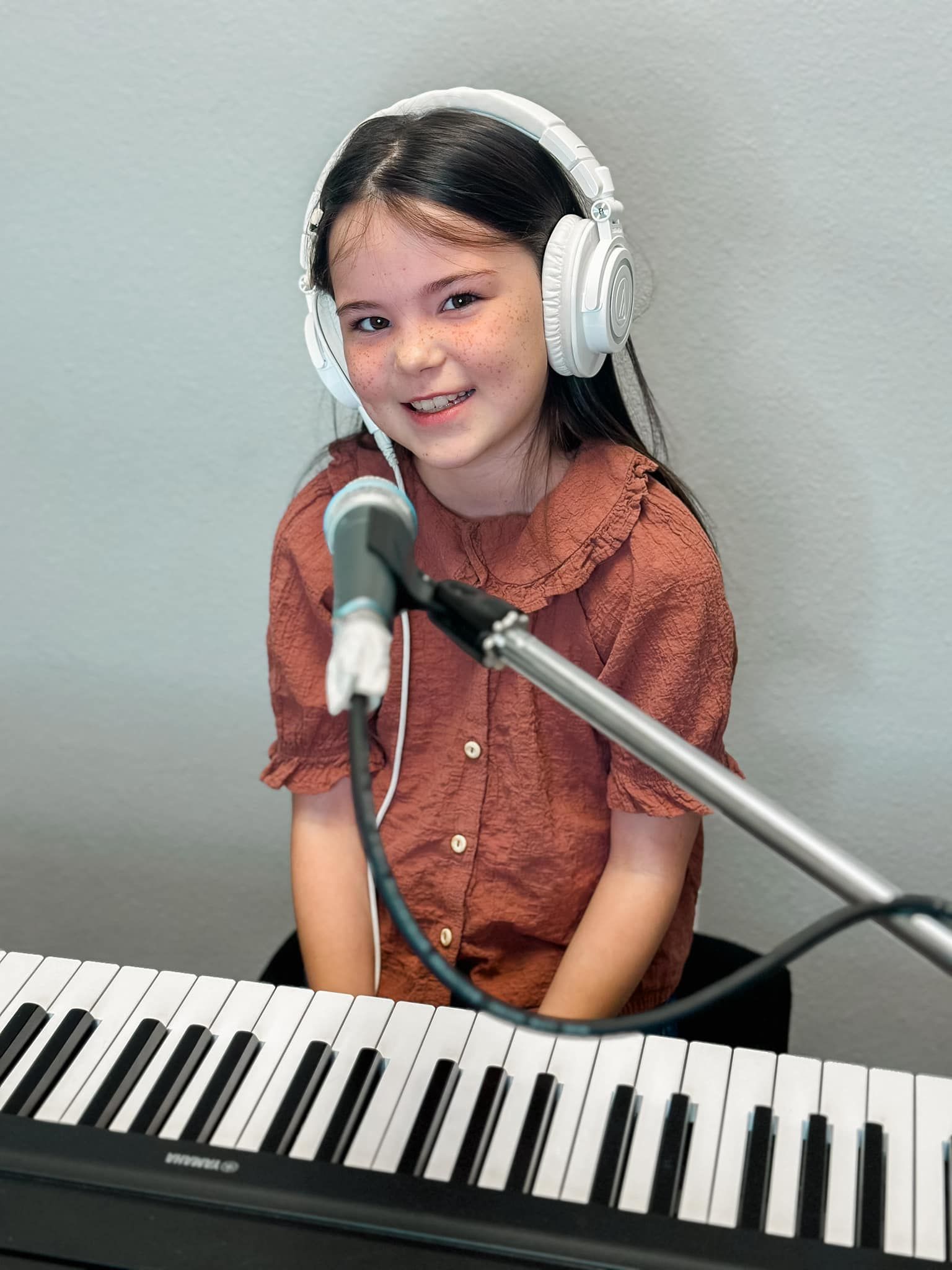 A young girl wearing headphones is playing a keyboard