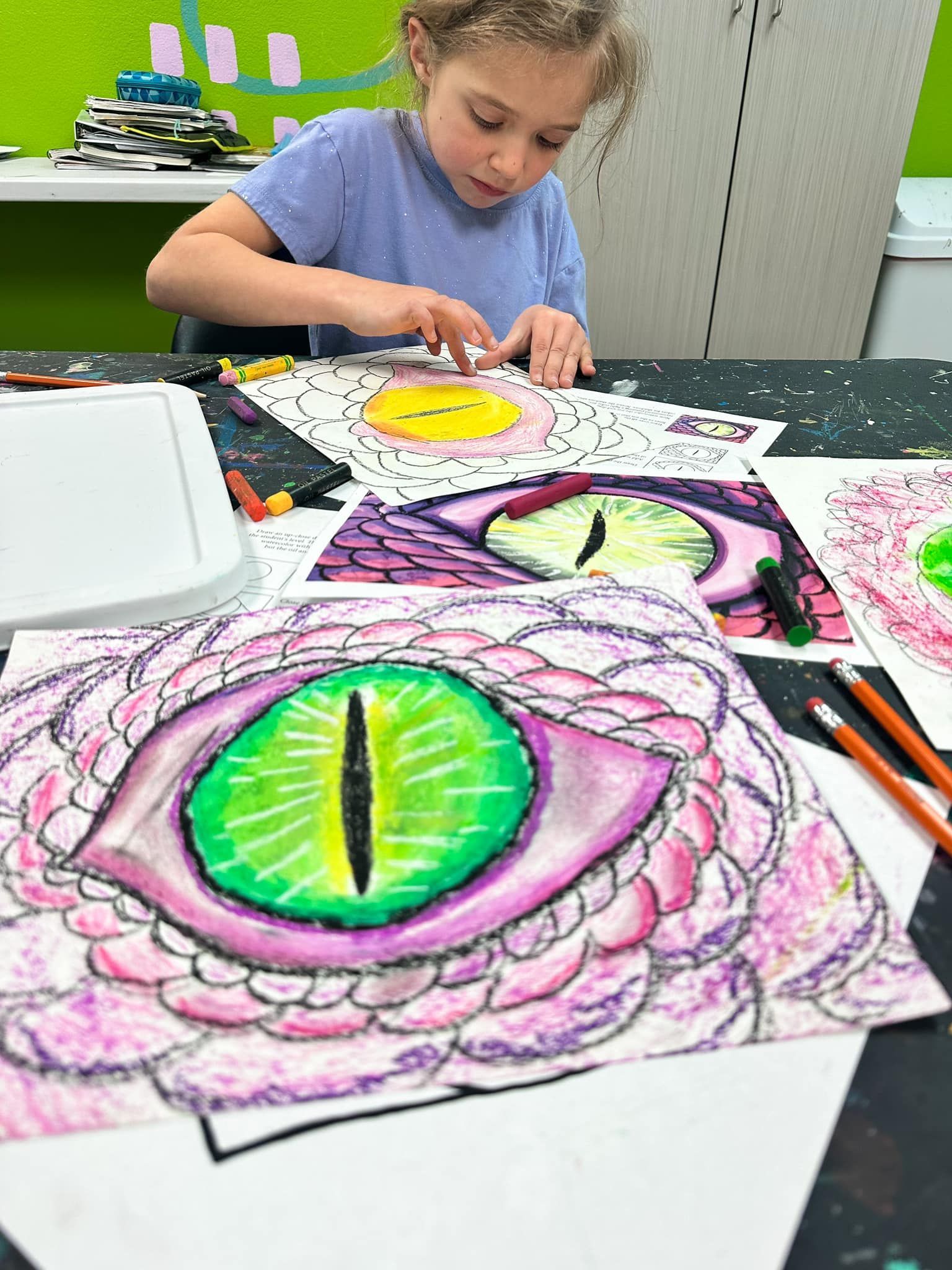 A young girl is sitting at a table drawing a dragon 's eye.