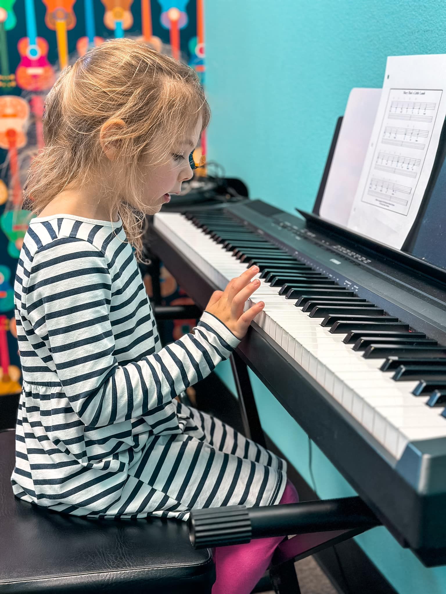 A little girl in a striped dress is playing a piano.