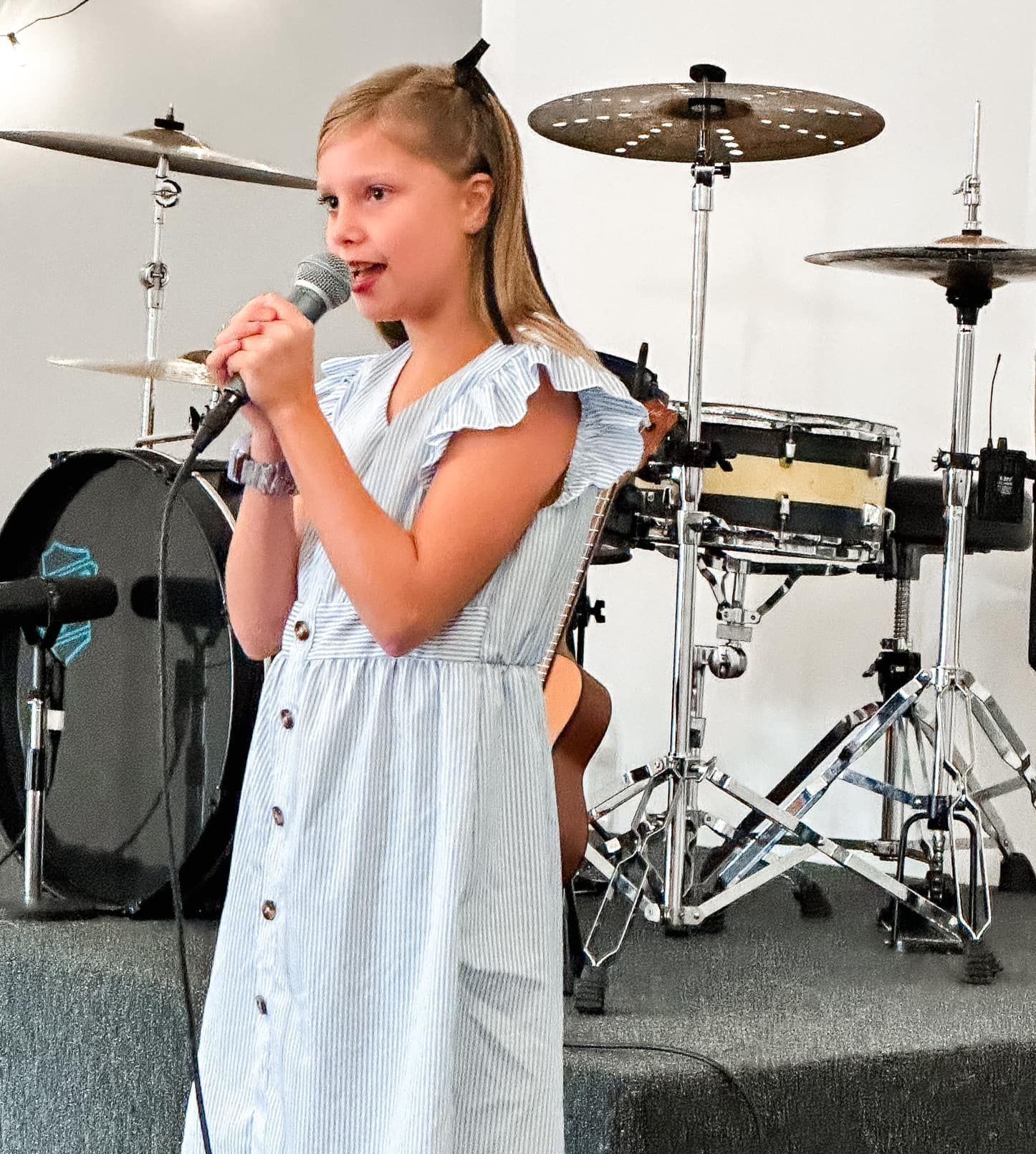 A young girl singing into a microphone in front of a drum set