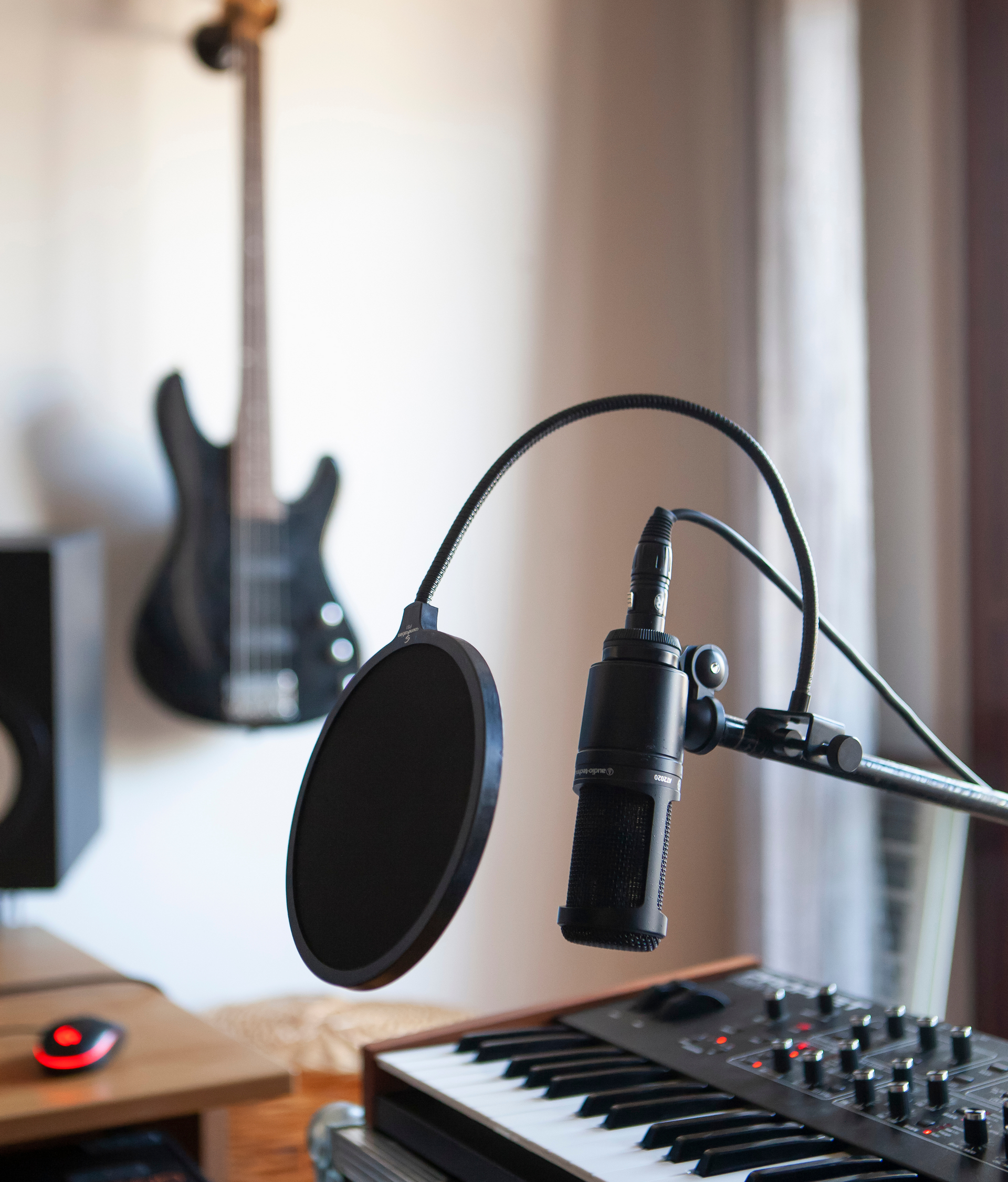 A microphone is sitting on top of a keyboard with a guitar in the background